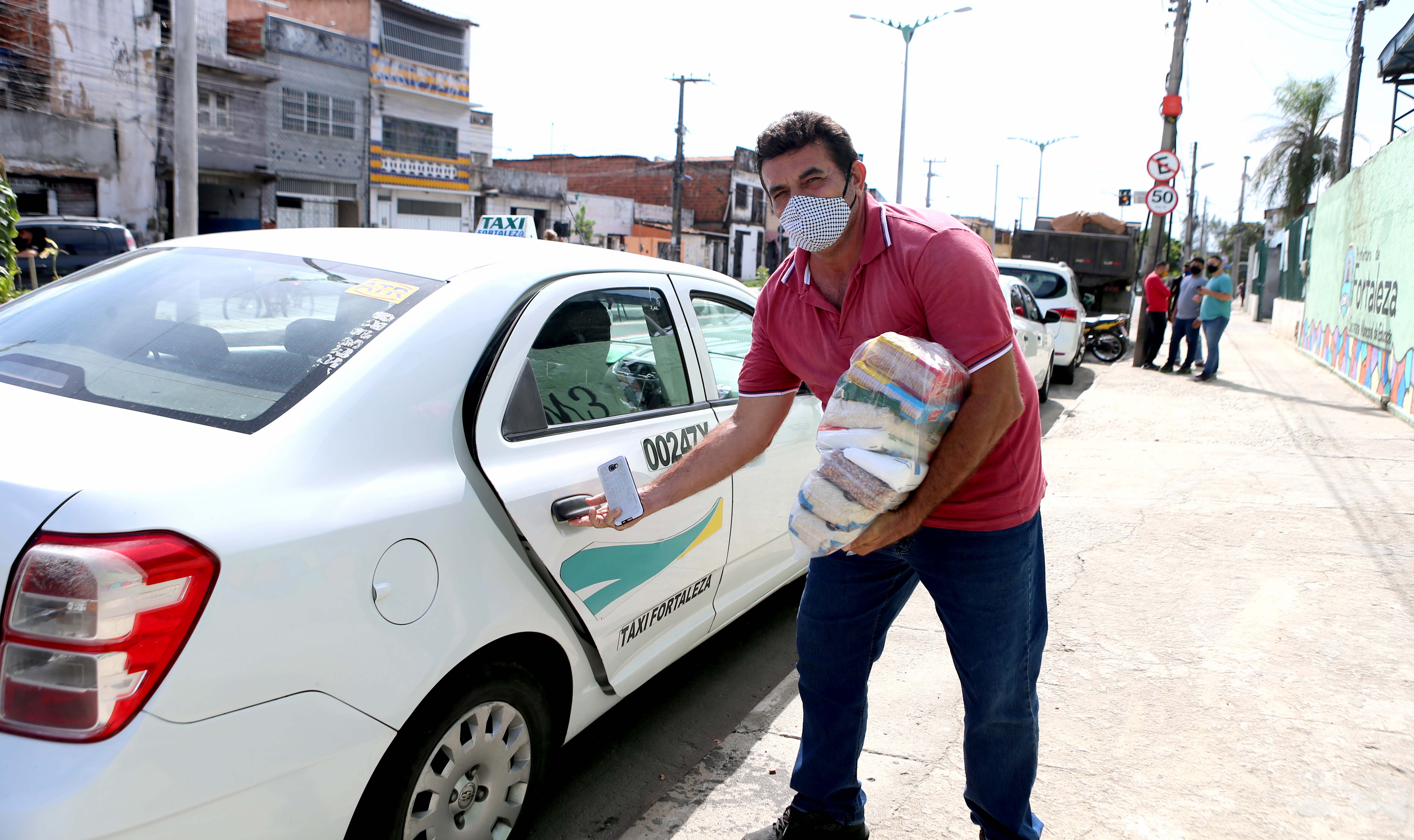 uma taxista coloca uma cesta básica no banco traseiro de seu carro